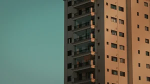 Prédio residencial alto ao pôr do sol, com janelas e varandas em destaque e uma fachada de cor clara, criando contraste com o céu azul ao fundo.