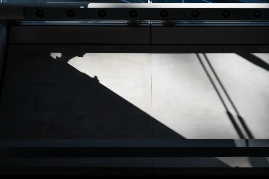 Close em uma impressora industrial, com uma área de impressão iluminada e detalhes de cabeçote e trilhos metálicos, mostrando o processo de impressão.