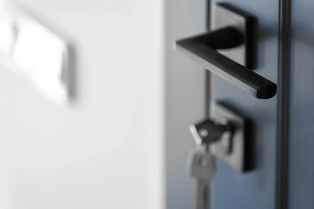 Detalhe de uma porta de vidro com fechadura e maçaneta ao lado, com aparência fosca e fundo desfocado, em ambiente interno moderno.